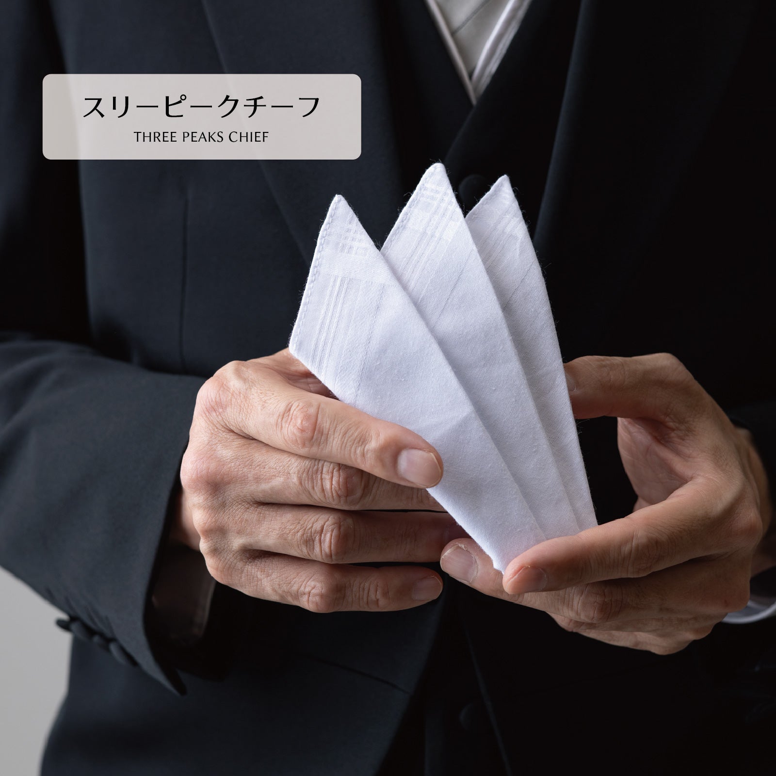 白いスリーピークのポケットチーフを両手で広げる様子
