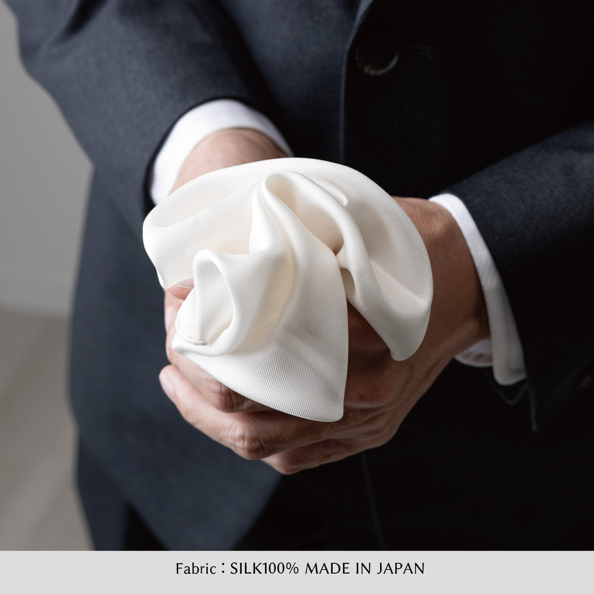 ホワイトのシルクチーフ、しわのある布を手で包む